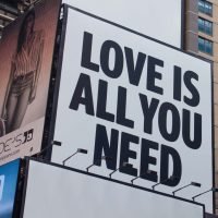Large city billboard reads 'Love Is All You Need' in New York City street.